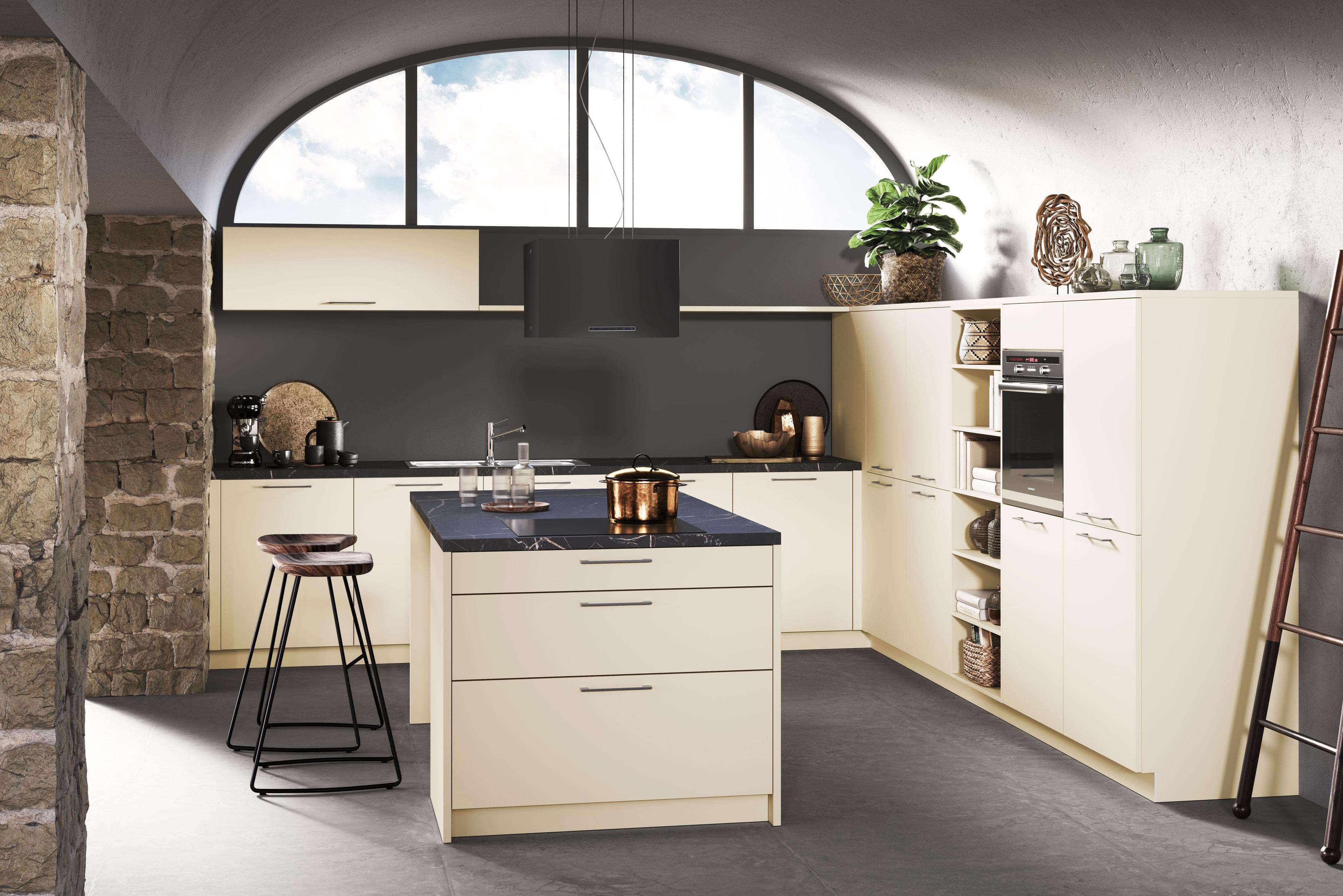 Häcker Küche in Creme/Magnolie mit dunkler Arbeitsplatte und kleiner Kücheninsel, kombiniert mit schwarzer Wandfläche und großem Rundbogenfenster.