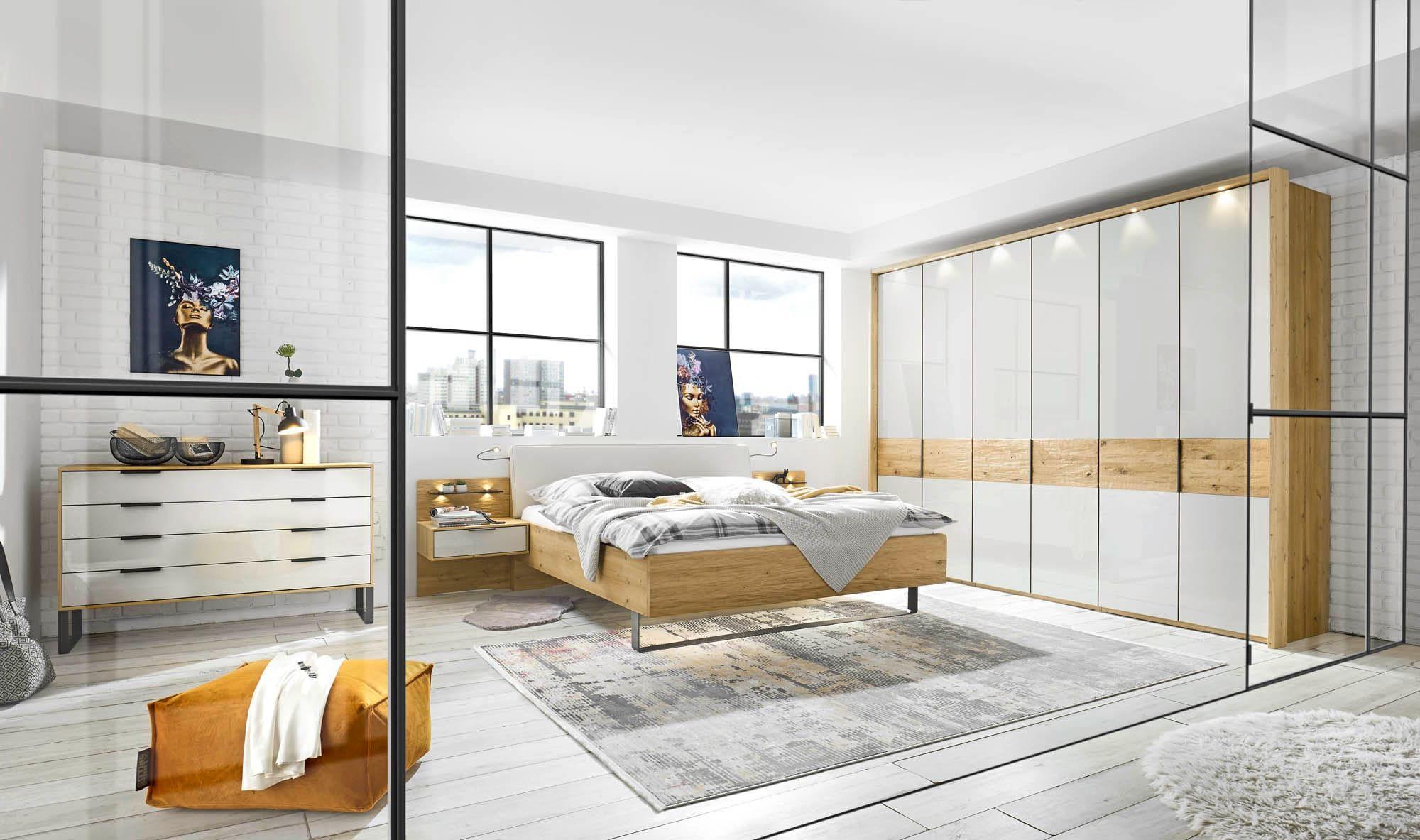 Calpe Calina Schlafzimmer-Programm in Eiche und Weiß mit Doppelbett, großem Drehtürenschrank mit Glasfronten und Kommode in hellem Loft mit Industriefenstern