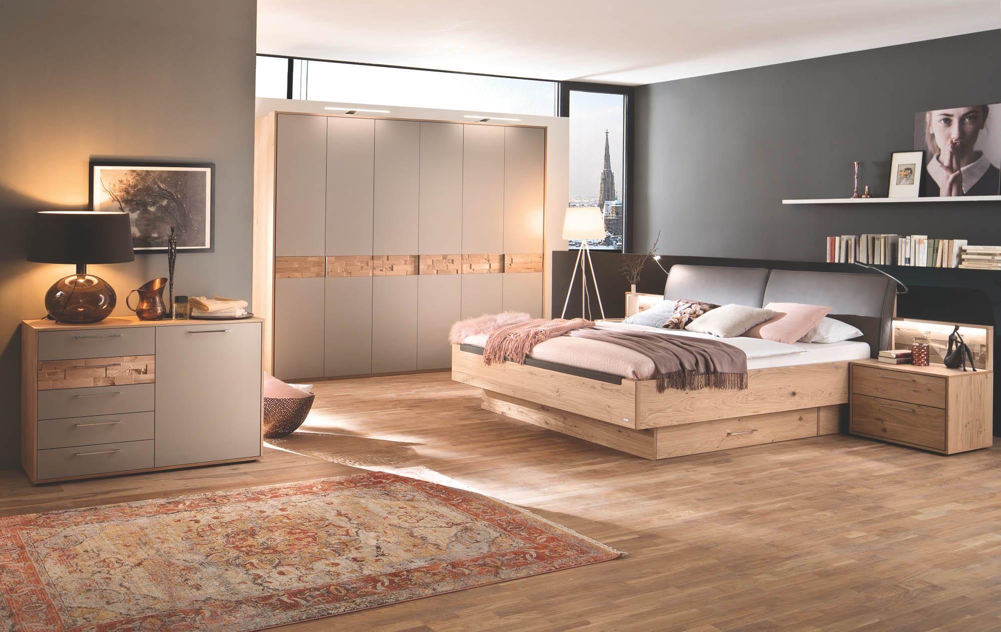 Casada Capena Schlafzimmer in Eiche und Taupe mit Bett mit gepolstertem Kopfteil, beleuchteten Nachttischen, Drehtürenschrank mit Holzakzenten und Kommode vor anthrazitfarbener Wand