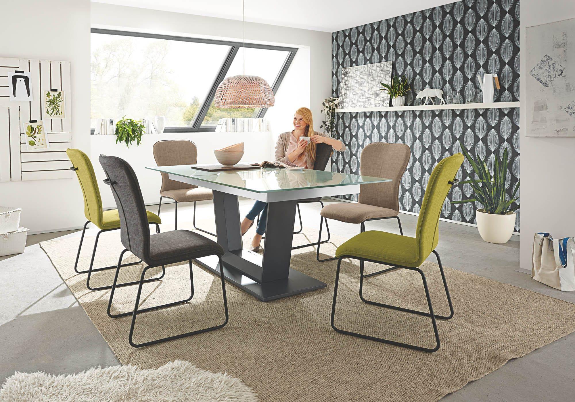 Crazy Essgruppe mit Glastisch auf dunklem Säulenfuß und bunten Kufenstühlen in Grün, Grau und Beige – Frau genießt Kaffee im modernen Essbereich mit Dachschräge