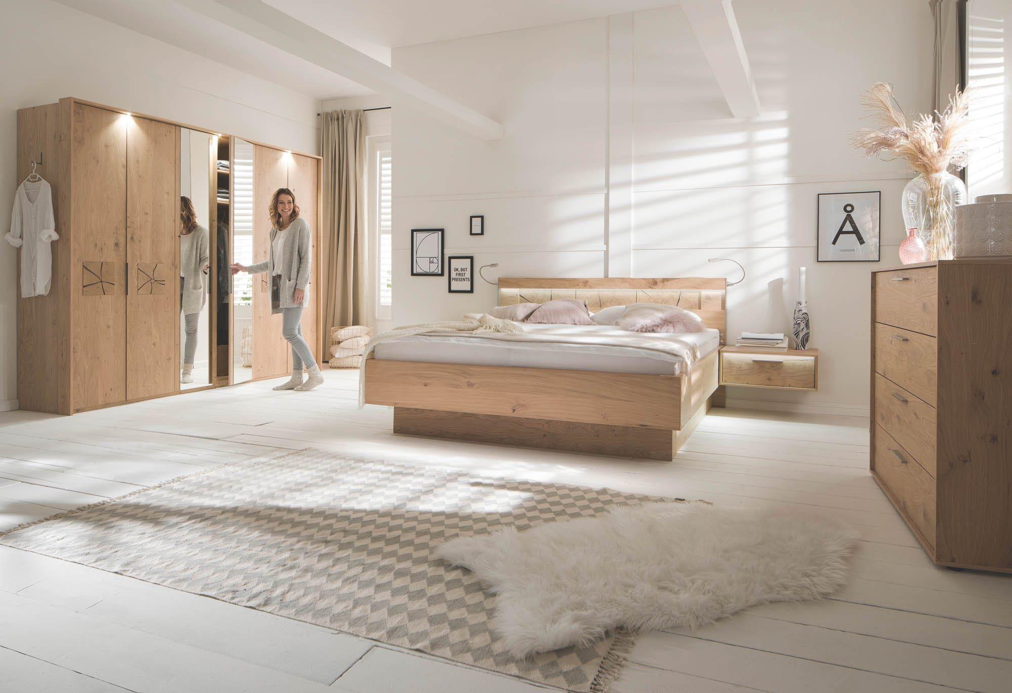 Freundlich helles Schlafzimmer mit Massivholz-Bettanlage, passendem Kleiderschrank mit Spiegelelement, Nachttisch und Kommode aus Holz; dezente Deko und viel Tageslicht