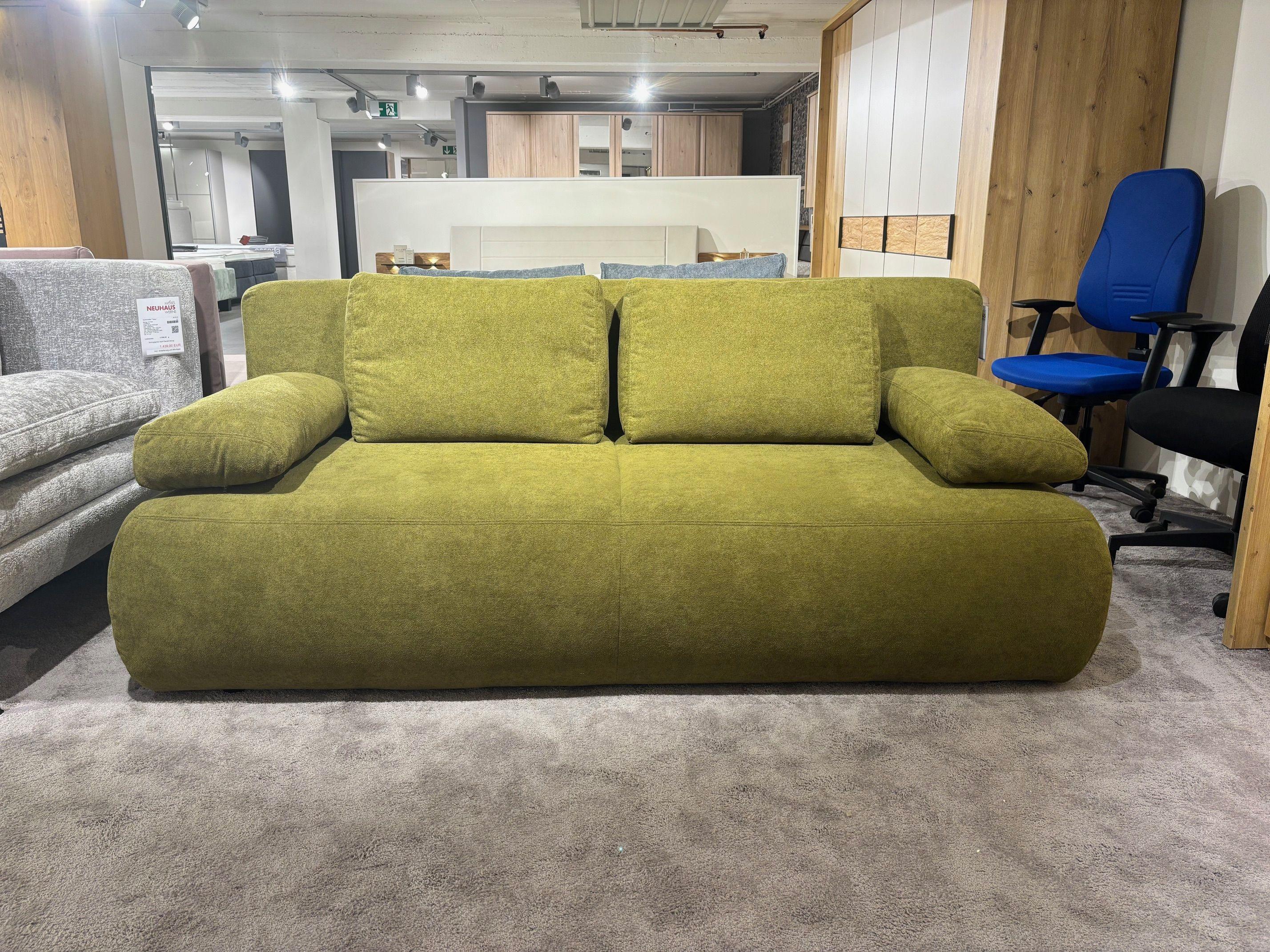 Grünes Stoffsofa mit zwei Rückenkissen und breiten Armlehnen in der Ausstellung.