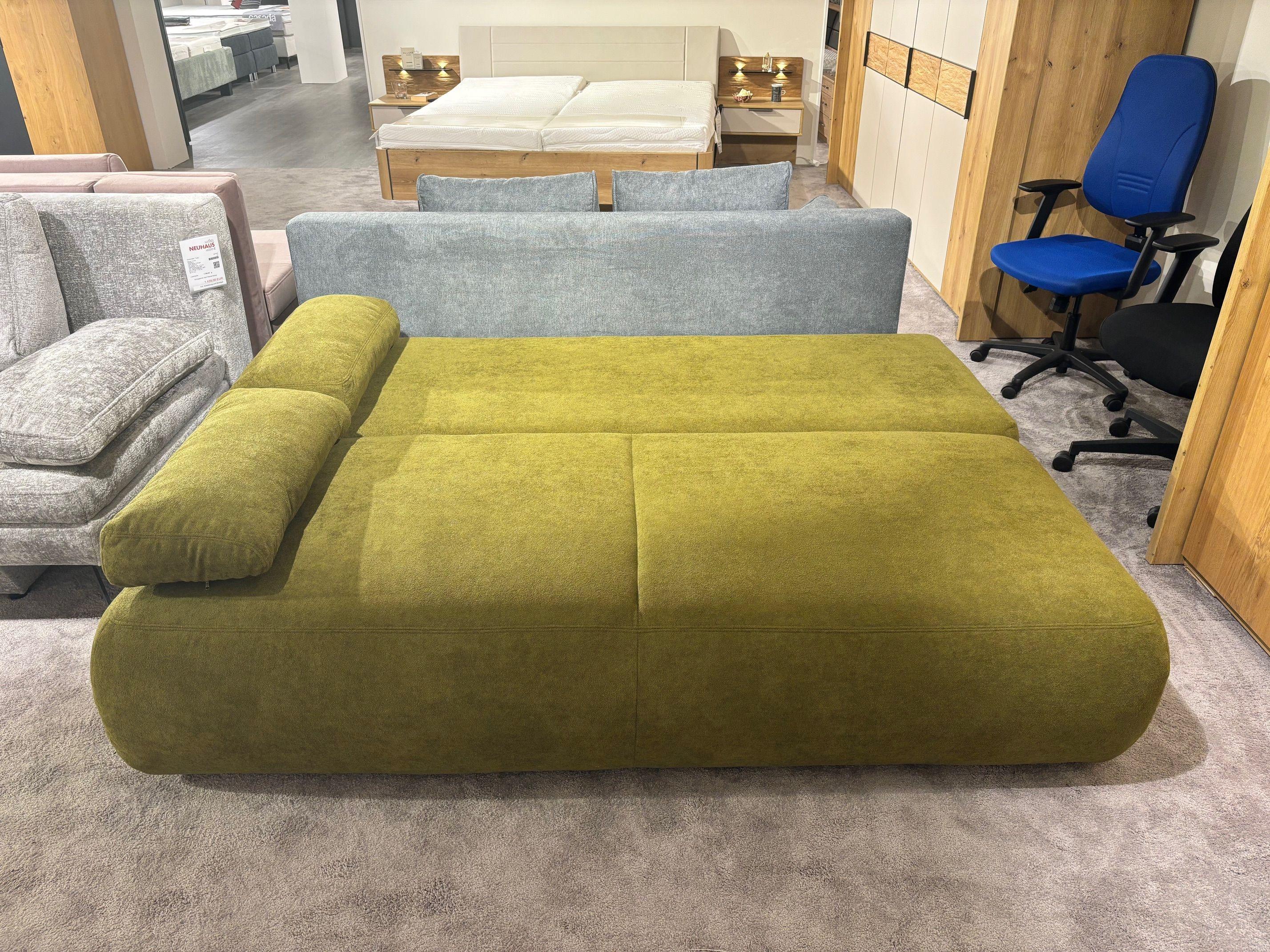 Grünes Sofa als Schlafsofa ausgeklappt, große Liegefläche in der Ausstellung.