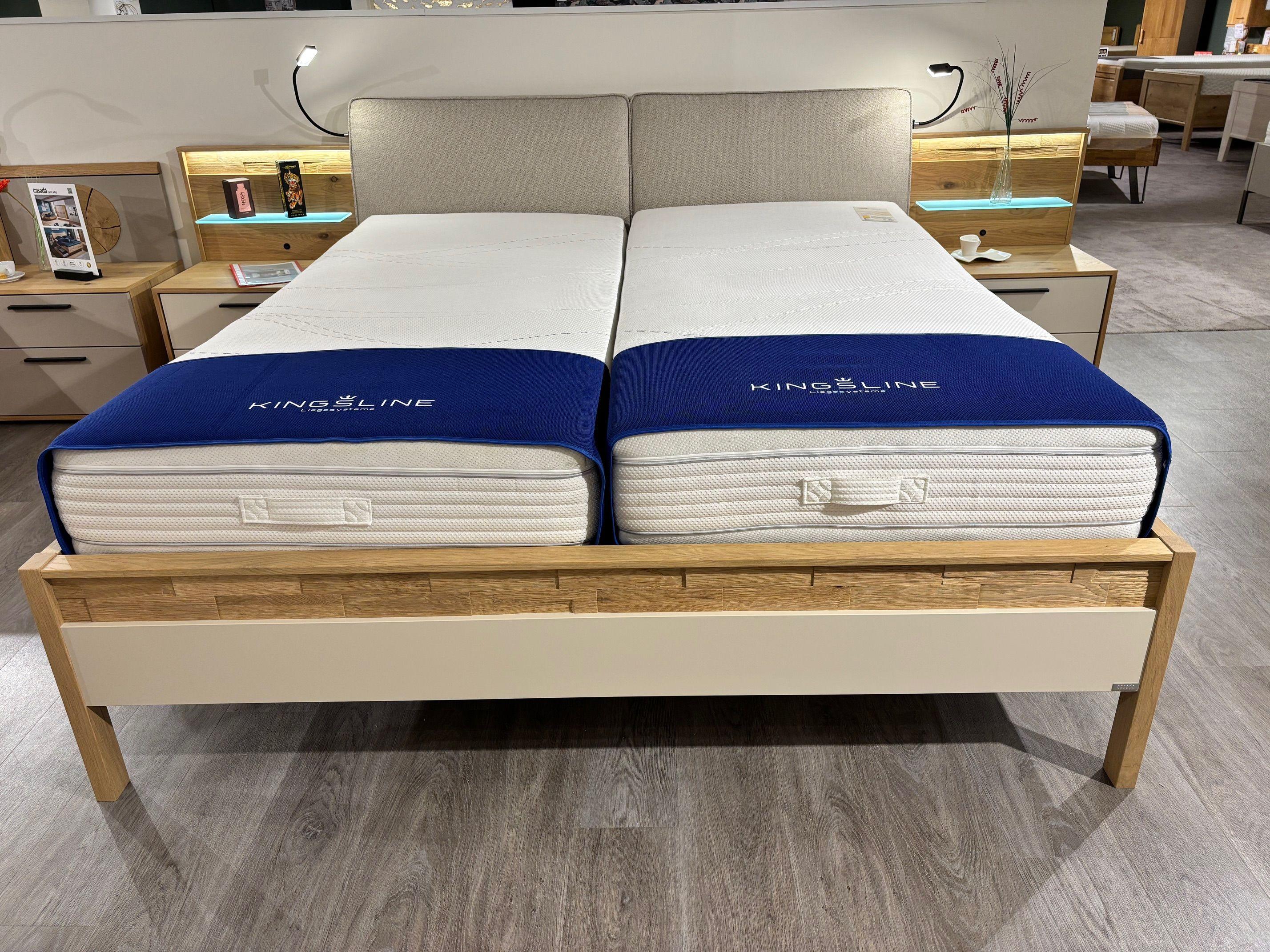 Doppelbett in Eiche mit zwei Kingsline-Matratzen, gepolstertem Kopfteil und beleuchteten Nachttischen in Frontansicht.