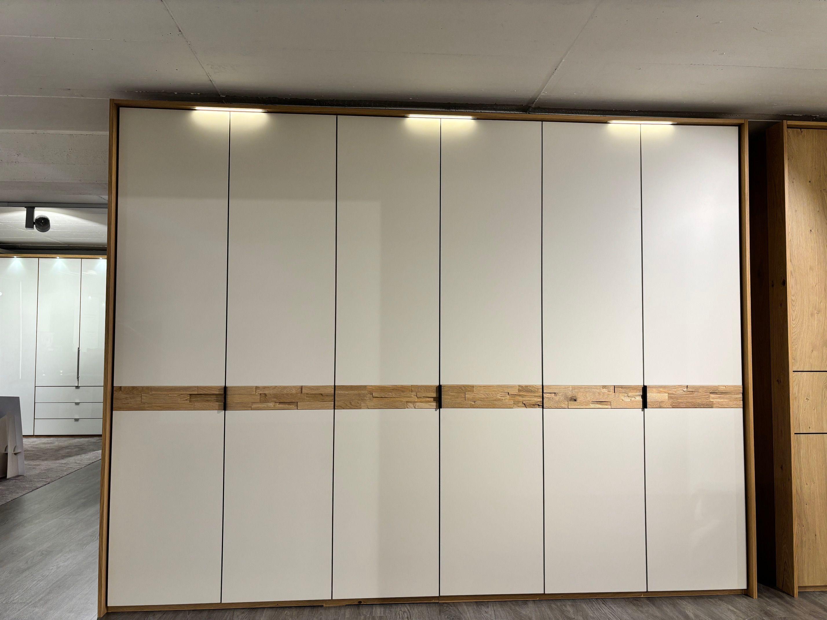 Großer Drehtürenschrank in Weiß Hochglanz mit Eiche-Spaltholz-Akzentleiste und integrierter Beleuchtung, sechstürig.