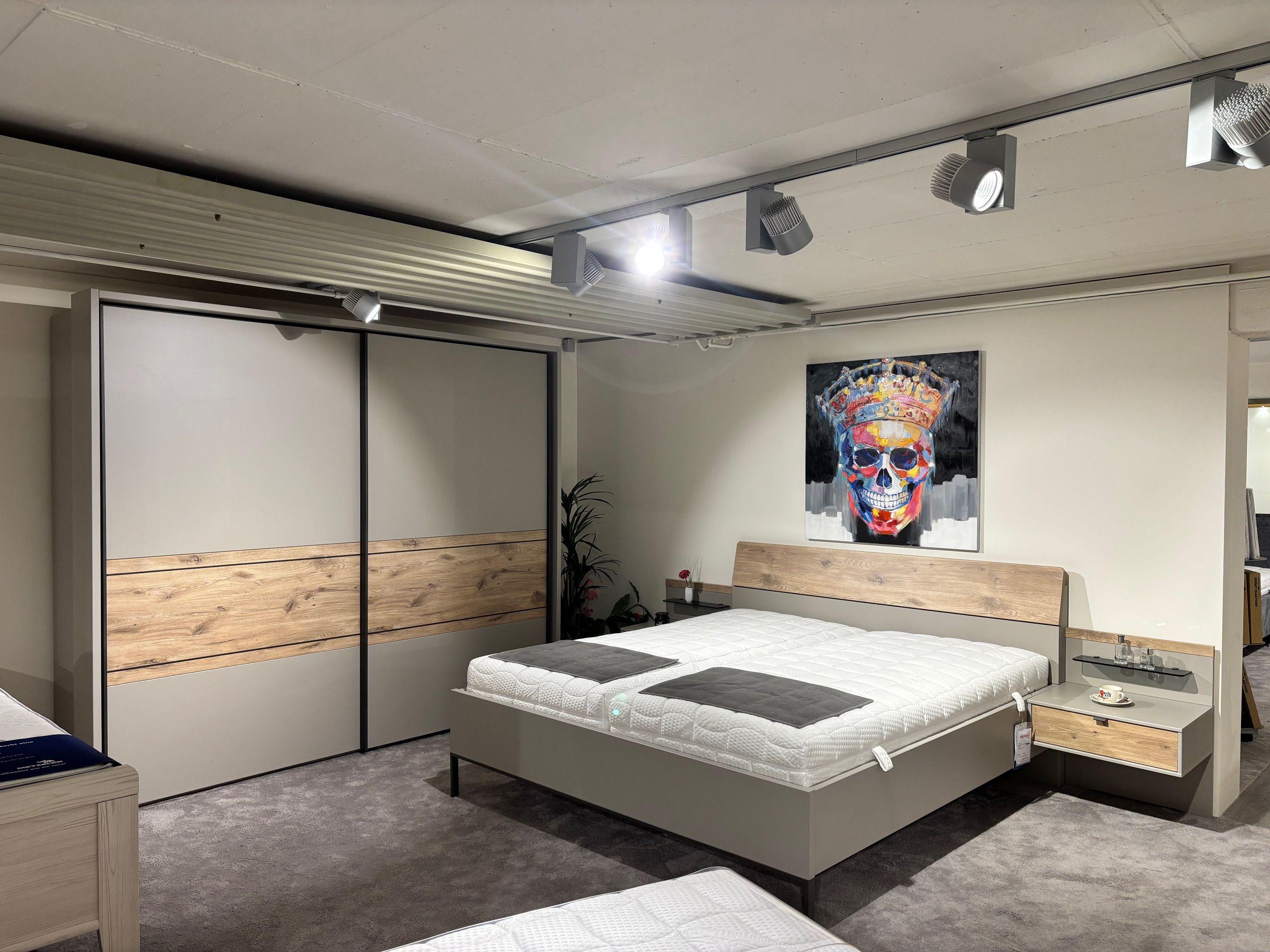 Schlafzimmer-Set mit Doppelbett, Nachttischen und Schwebetürenschrank in Grau mit Eiche-Absetzungen im Ausstellungsraum.