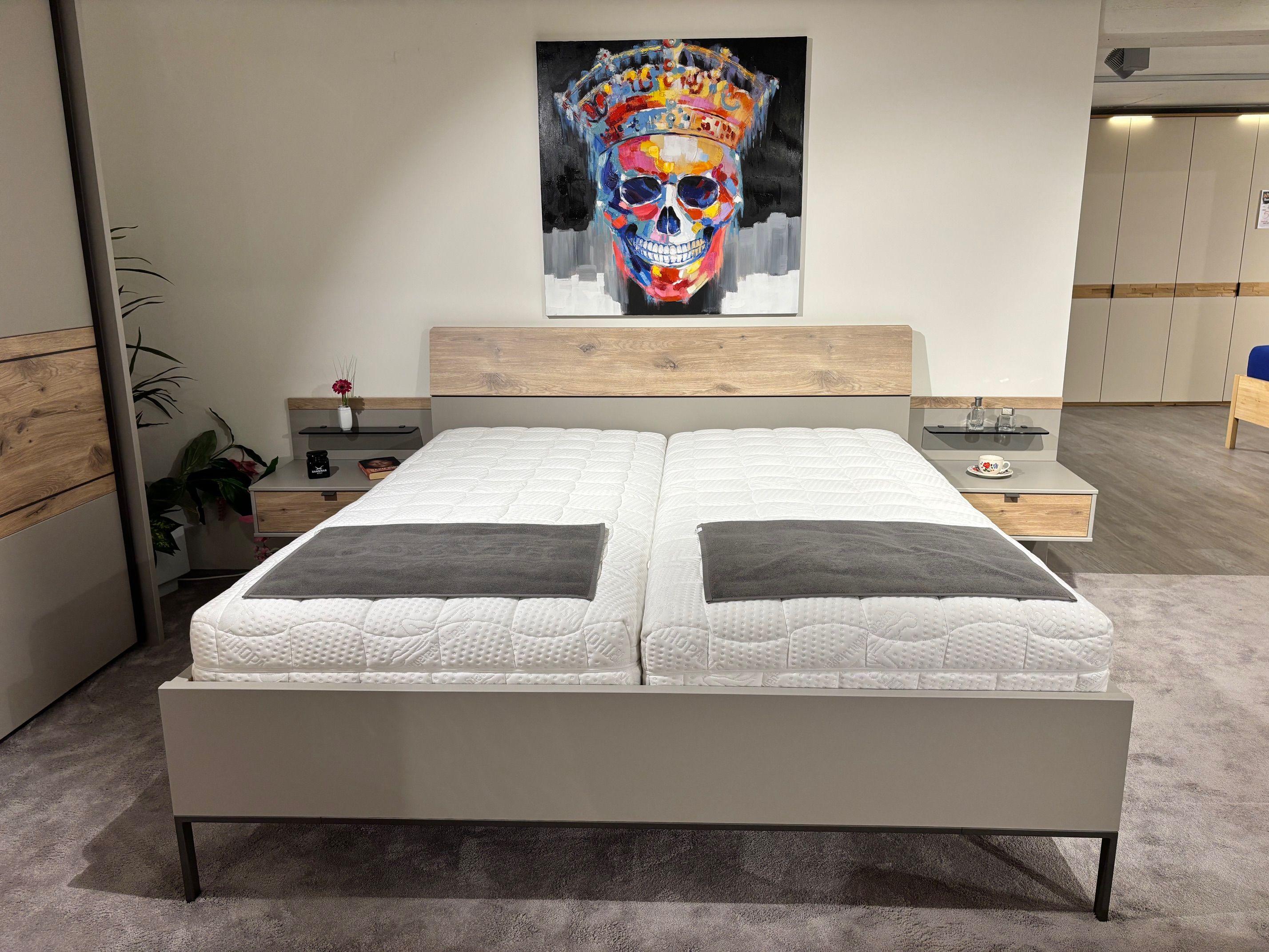 Doppelbett in Grau mit Eiche-Kopfteil, zwei Matratzen und passenden Nachttischen mit Glasablagen in Frontansicht.