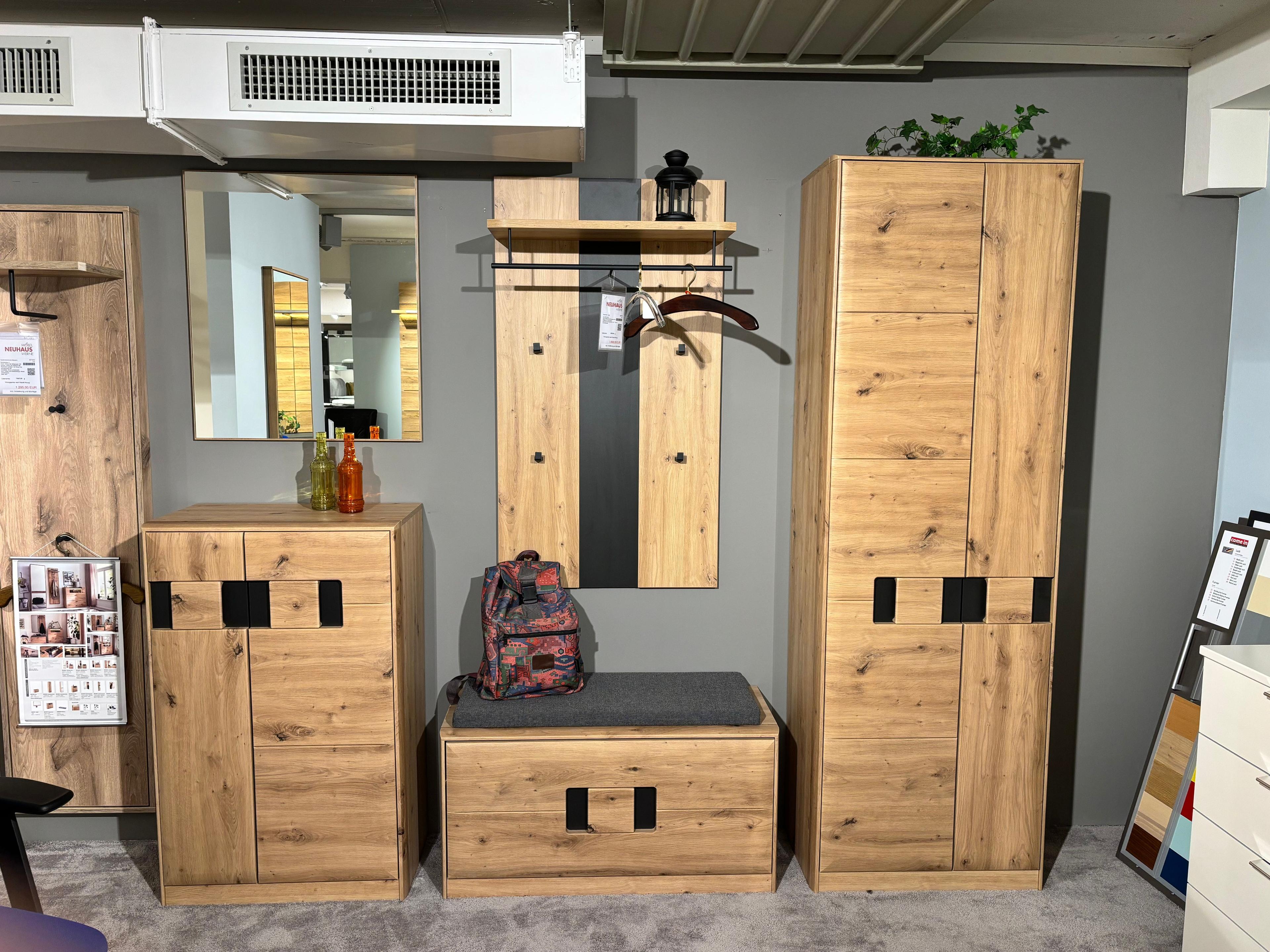 Garderobenmöbel-Set aus Holz mit schwarzem Akzentgriff – bestehend aus Hochschrank, Kommode, Sitzbank, Wandpaneel mit Spiegel und Garderobenhaken – ausgestellt in einem Möbelhaus.